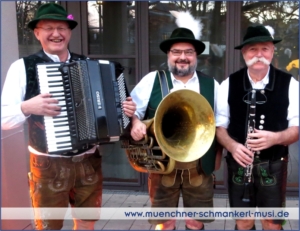 Drei Musiker der Münchner Schmankerl Musi in traditioneller Lederhose und Tracht mit Akkordeon, Tuba und Klarinette bei einem Firmenevent in Bayern.